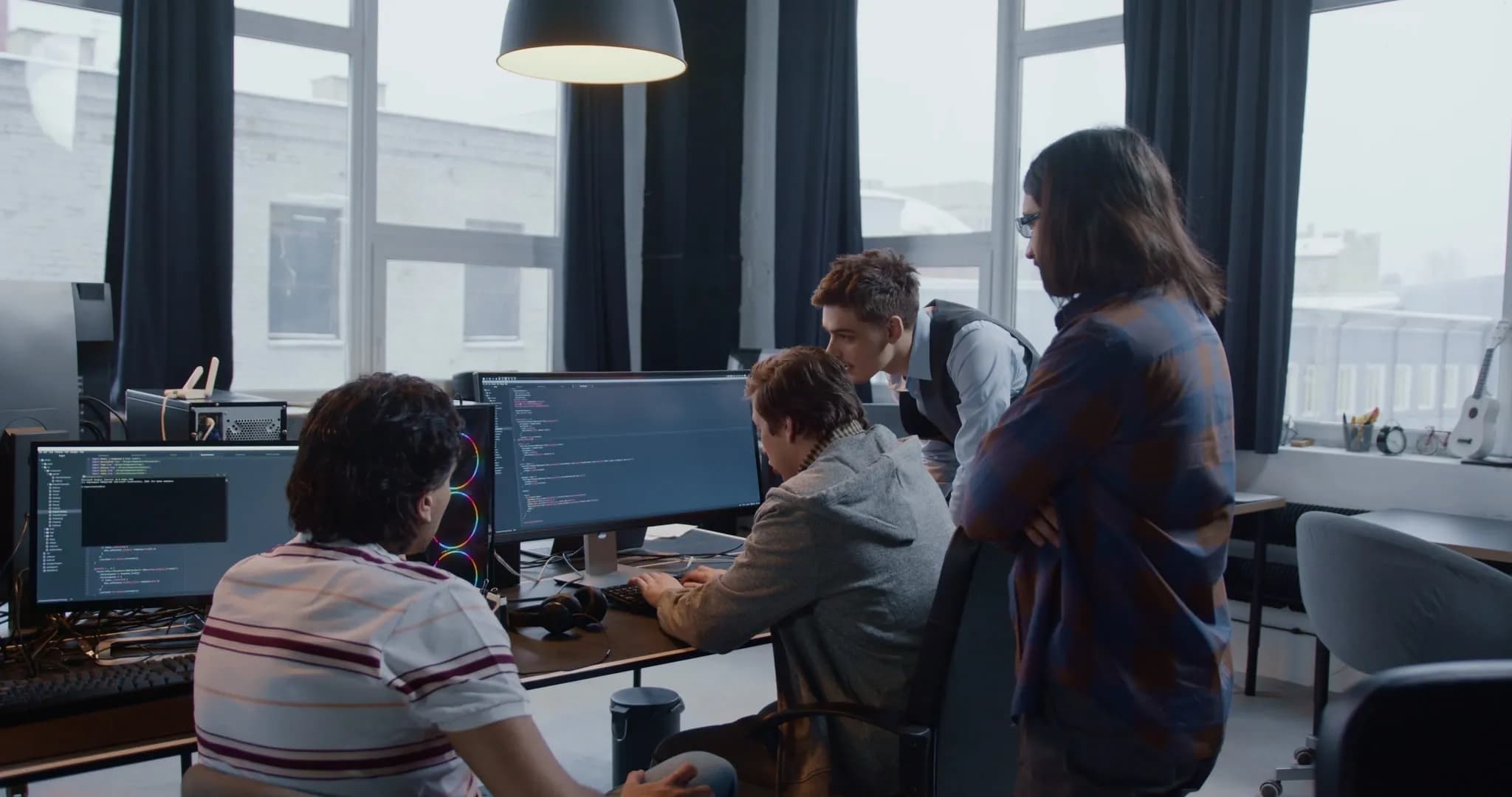 Developers reviewing code together on large monitors in a bright office.